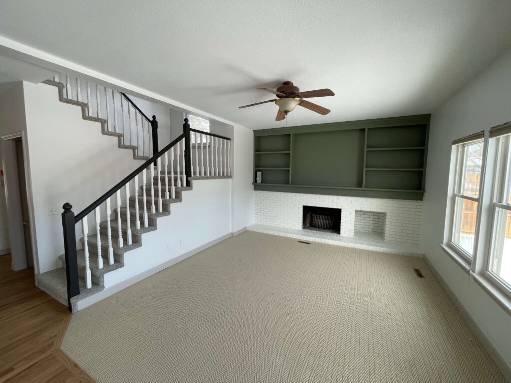 Completed interior painting project by Black Ridge Contracting in Des Moines Iowa showing freshly painted living room with white walls sage green built-in shelves black stair railing and brick fireplace